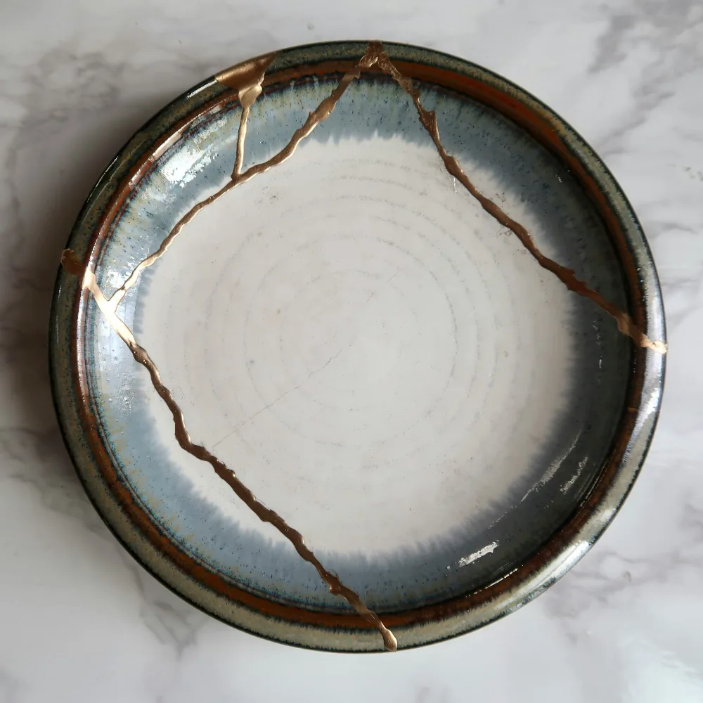 square cropped, close-up photo of a broken plate repaired with gold in kintsugi style (featured image: "Broken, Not Beyond Repair: A Creative Grief Workshop" mental health workshop)