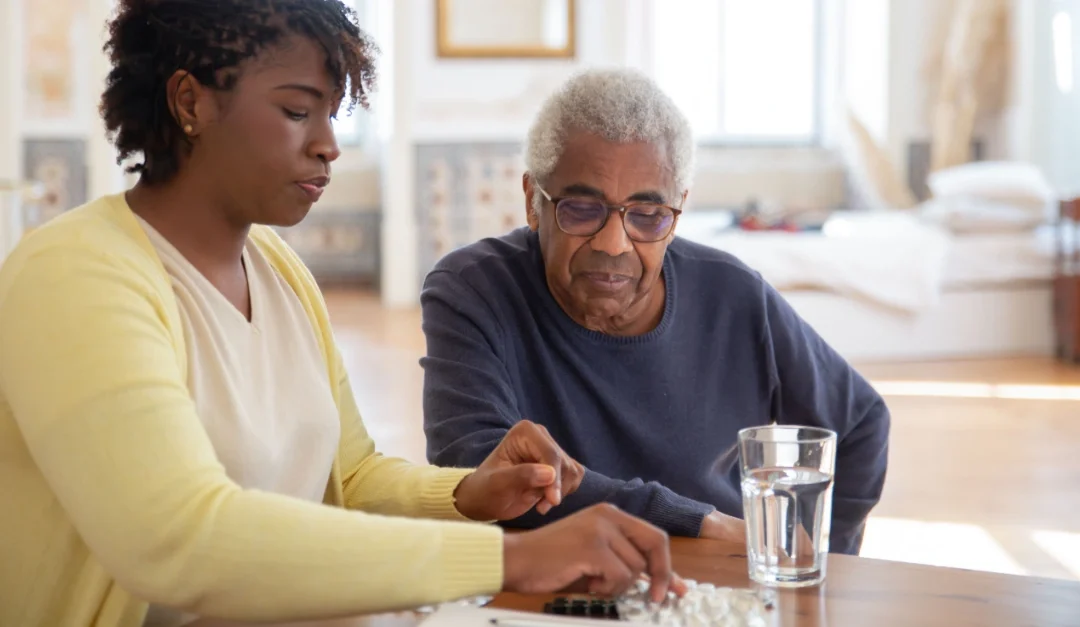photo of a woman helping her father with his medication at a kitchen table (featured image: "Caring for Others Without Losing Yourself: Therapy and Support for Caregivers" article)
