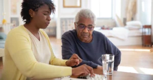 photo of a woman helping her father with his medication at a kitchen table (featured image: "Caring for Others Without Losing Yourself: Therapy and Support for Caregivers" article)